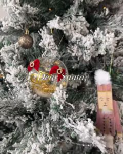 Nahaufnahme einer Weihnachtsbaumkugel an einem weißen Tannenbaum mit der Aufschrift Dear Santa
